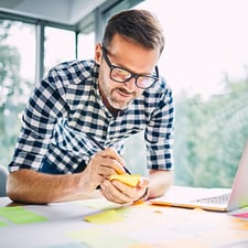 A business man writing down sticky notes on a desk