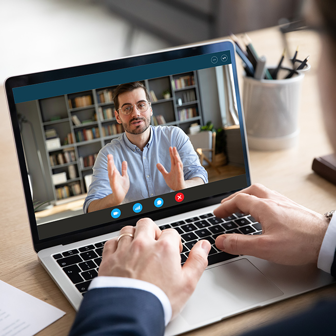 Two people video chatting with one on the screen of a laptop and the other facing the screen.
