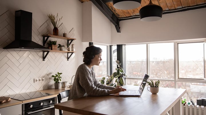 A woman in a kitchen typing on a laptop.