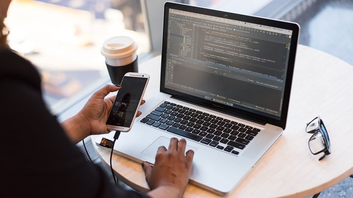 A woman holding her phone up sitting at her computer