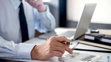 A man sitting at a desk entering numbers into a calculator